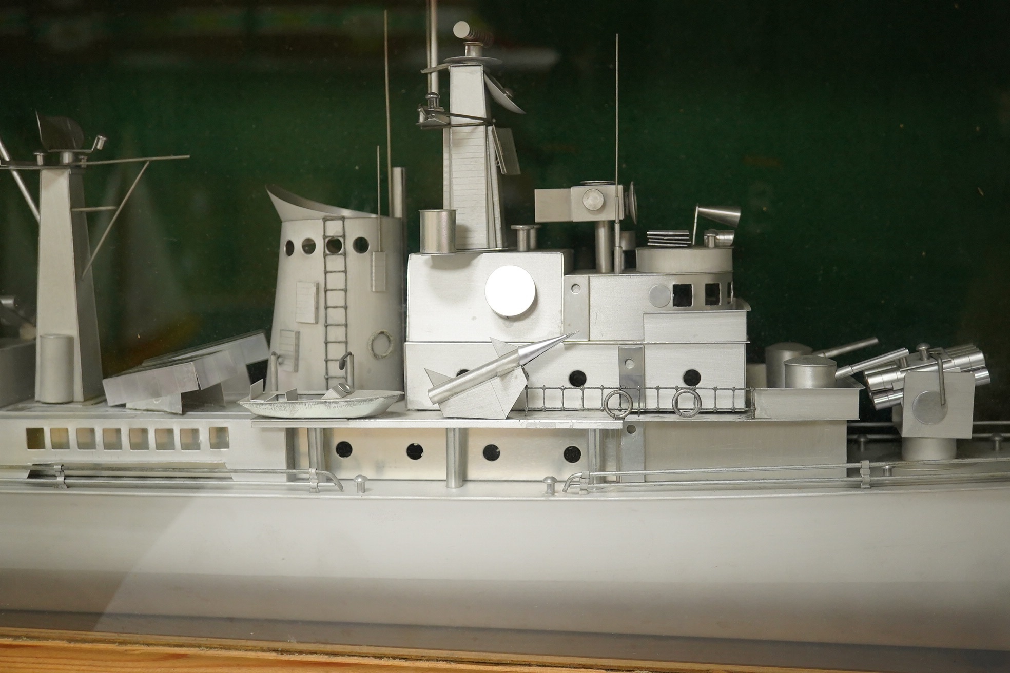 A pine cased aluminium model of a naval frigate, hull 86cm long, display case 96.5 x 18 x 36cm. Condition - good.